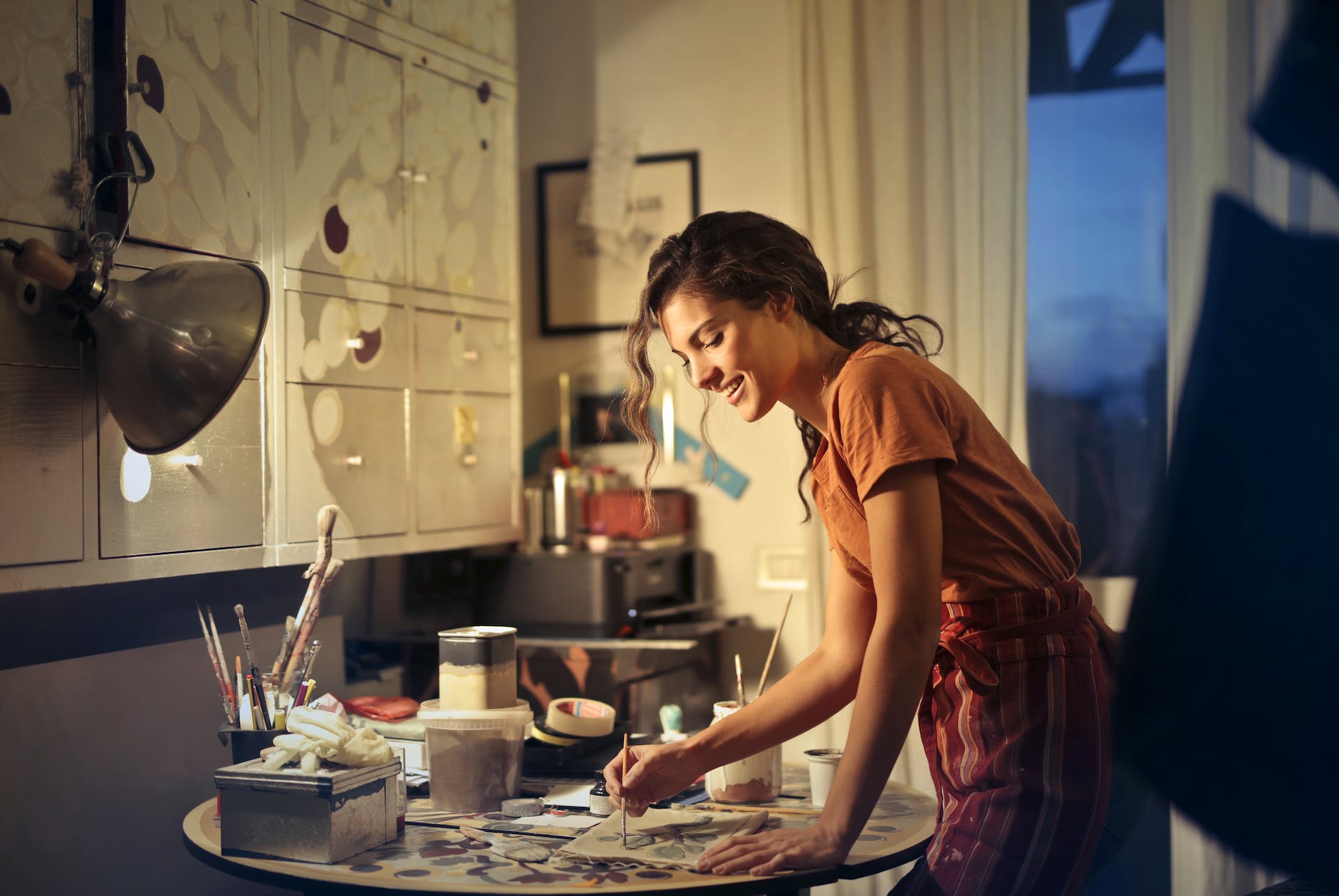 photo of woman painting while smiling and standing by the table
